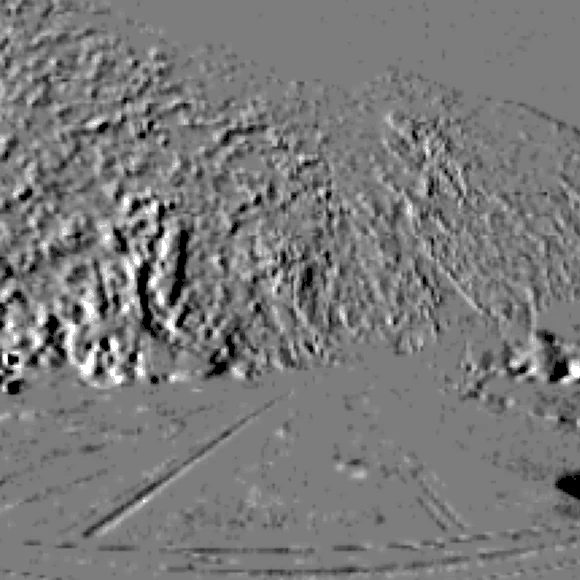 Event-camera frame of a road beside a hillside in daylight: rock texture, road markings and the horizon picked out against flat grey.